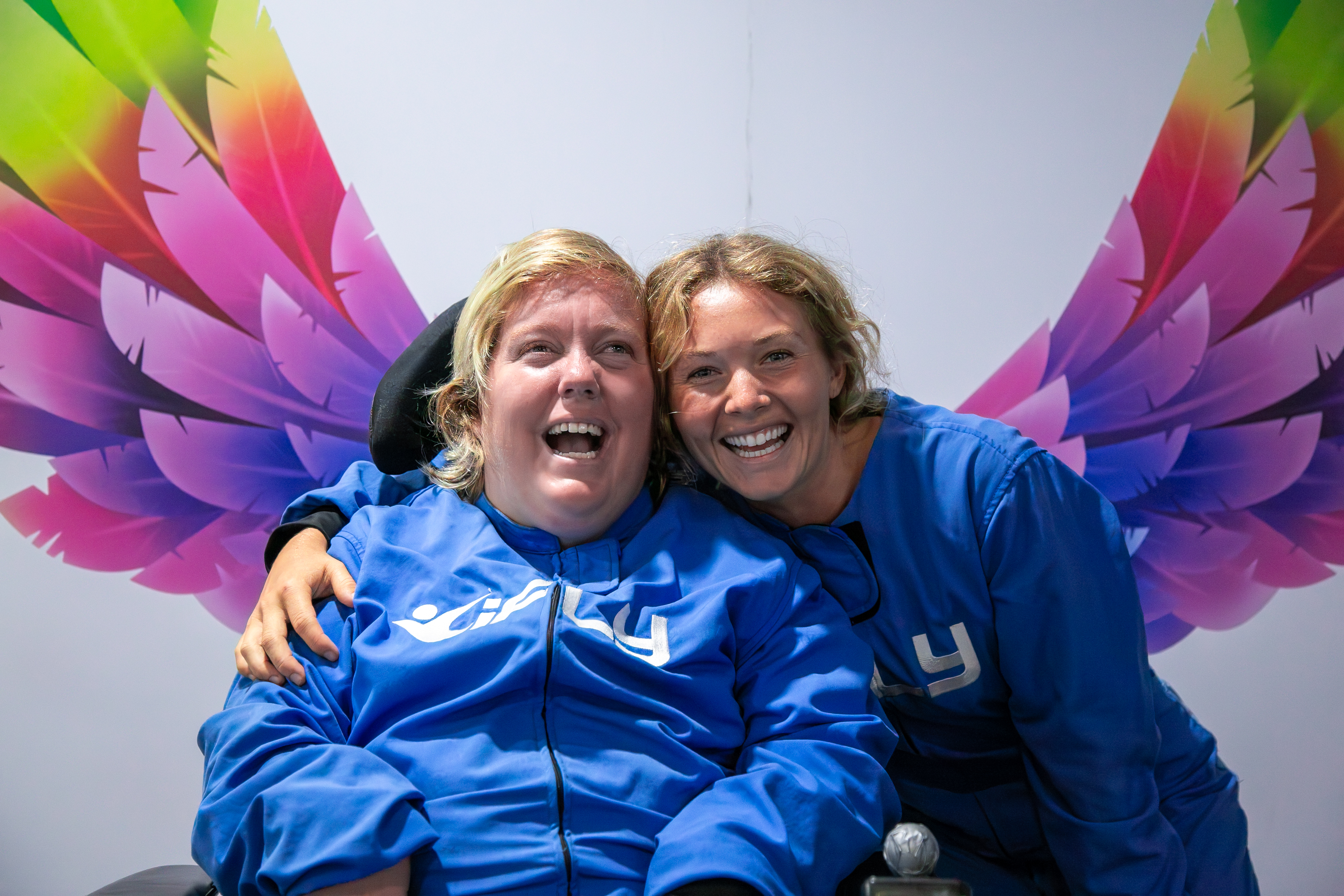 Two smiling people in blue flight suits in front of colourful wings