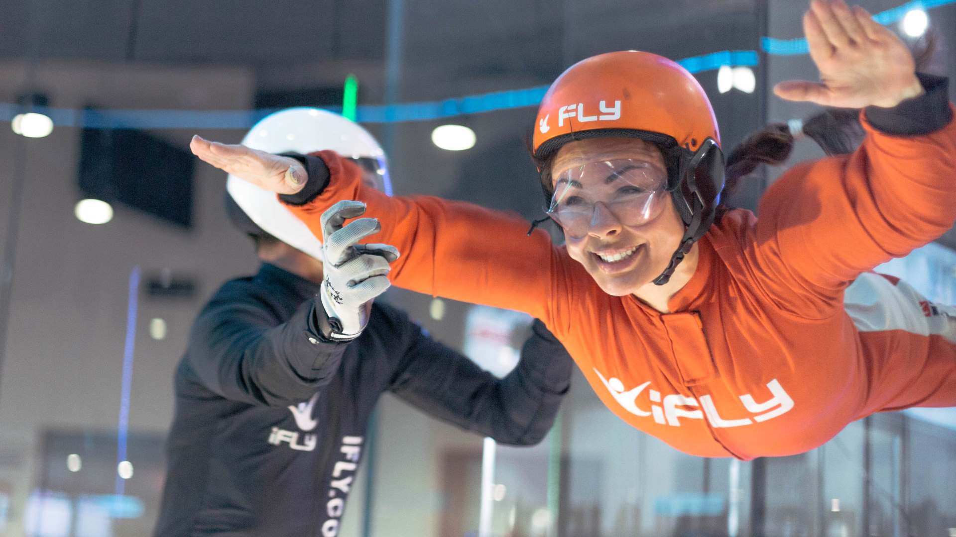 A woman in an orange jumpsuit flying with an instructor.