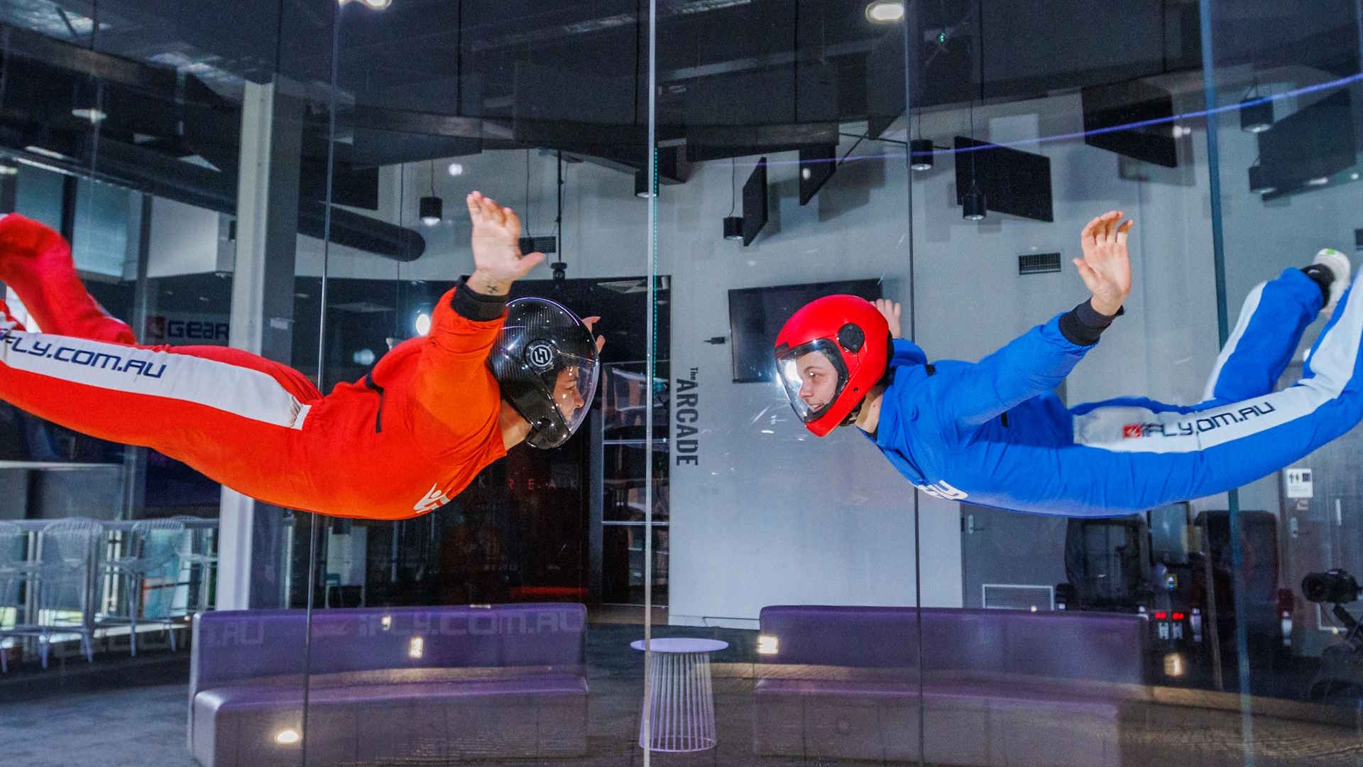 Two flyers in orange and blue jumpsuits flying and looking at each other