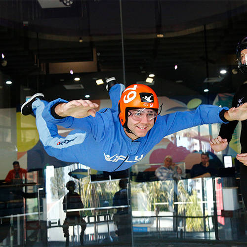 A smiling flyer floating in the wind tunnel with an instructor nearby