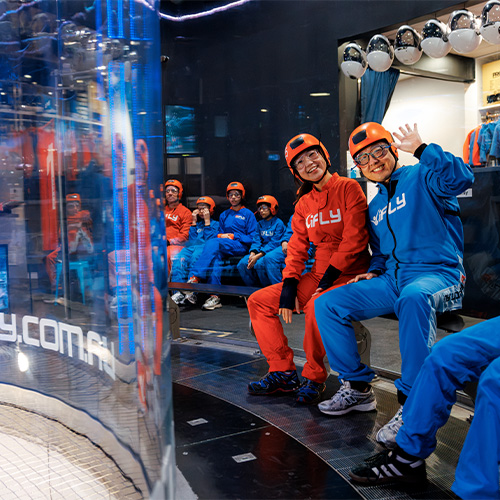 Flyers seated beside the wind tunnel smiling and waving
