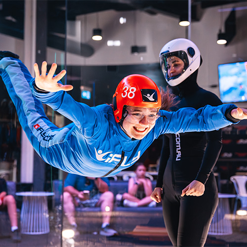 A smiling flyer supported by an instructor inside the wind tunnel
