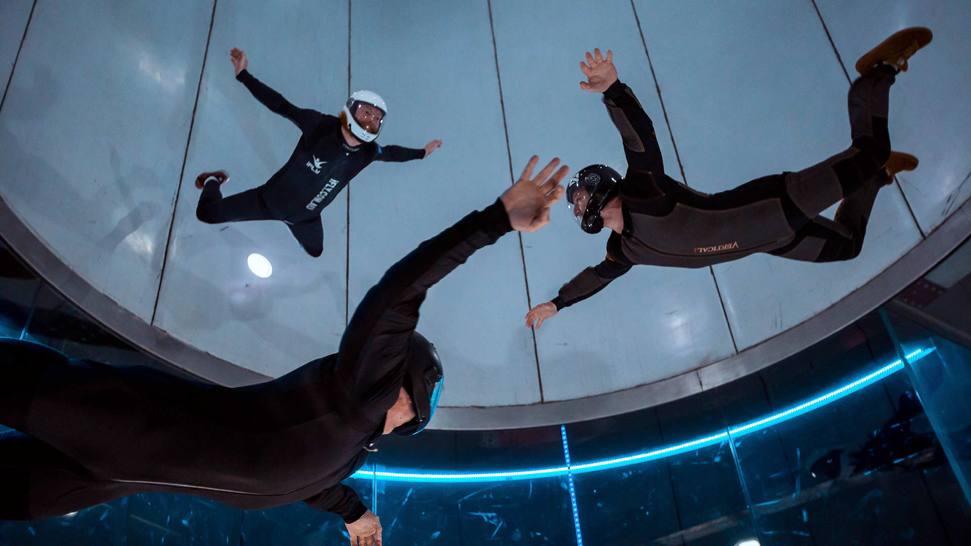 Three people flying in a wind tunnel wearing black jumpsuits